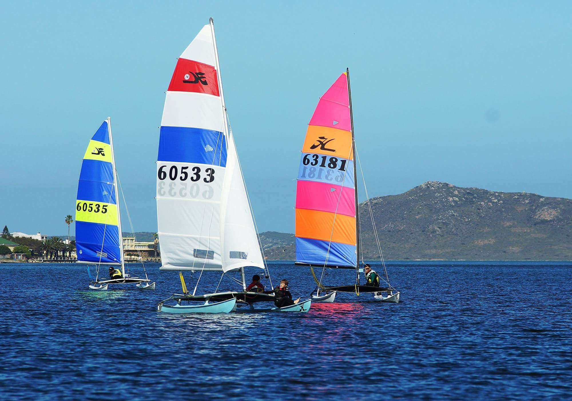 Three Hobie catamarans with colourful sails on a lagoon