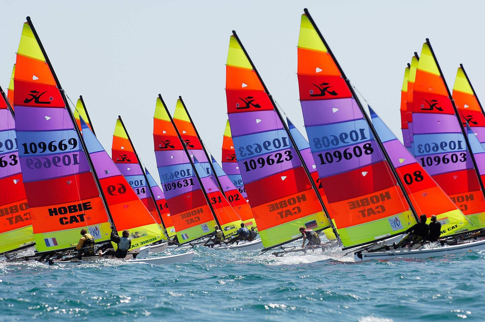 A fleet of Hobie 16s with rainbow sails racing side by side