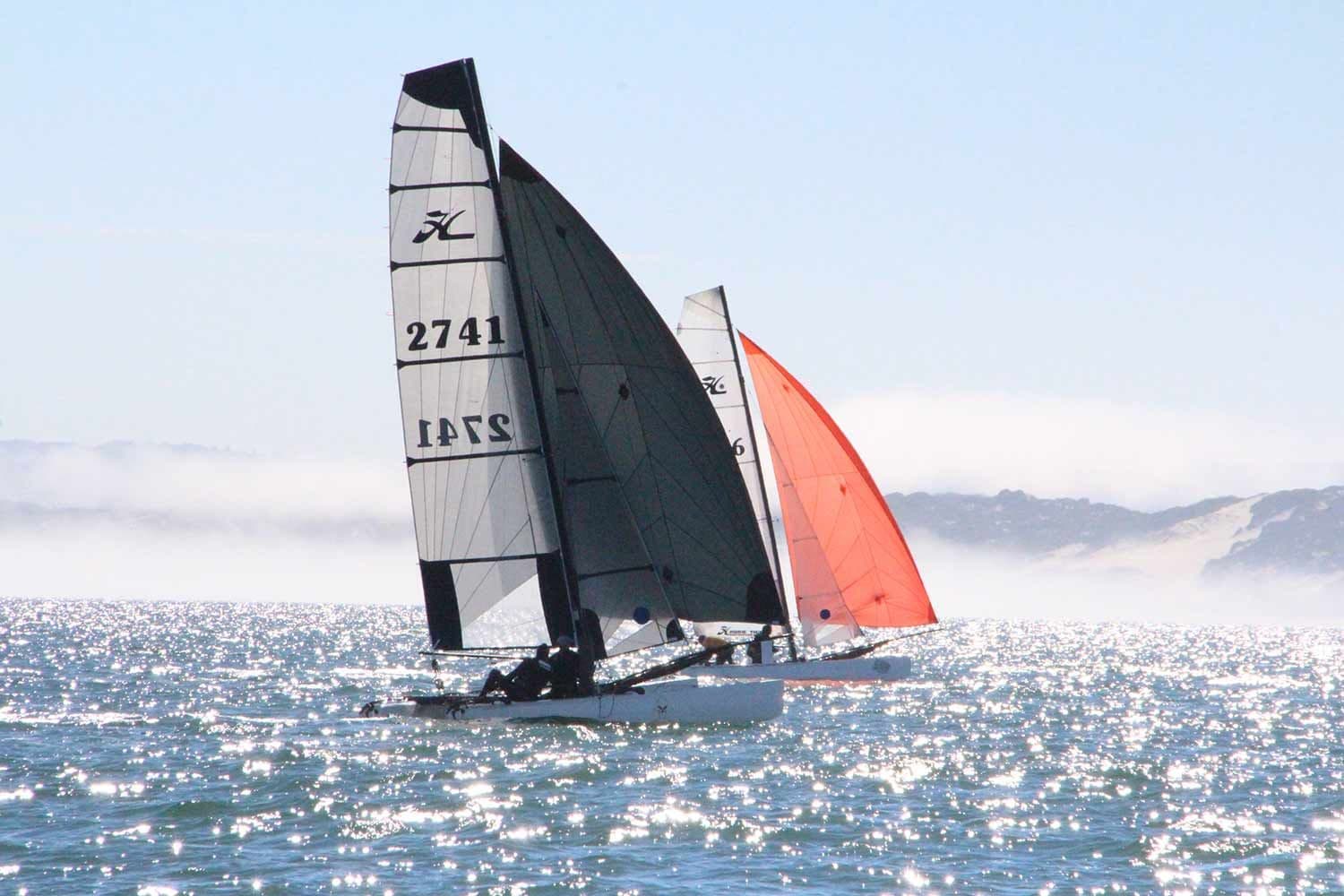 Two Hobie Tigers sailing on sparkling water, one flying an orange spinnaker