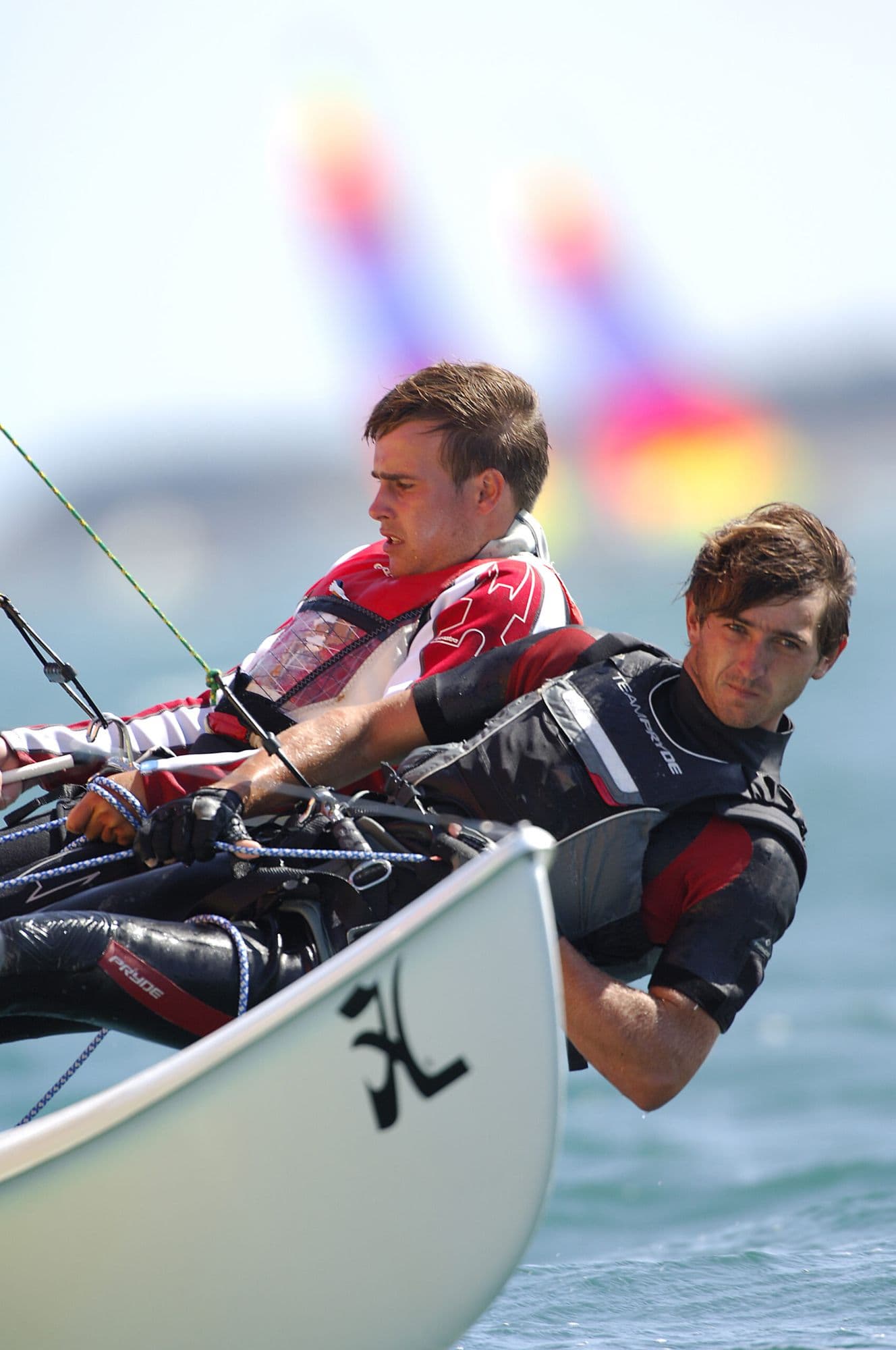 Two sailors hiking out on the trapeze of a Hobie, with rainbow sails behind